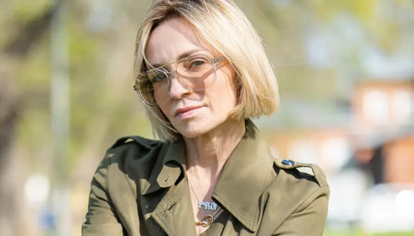 Anna Wyszkoni w okularach i zielonym płaszczu, na tle zieleni.