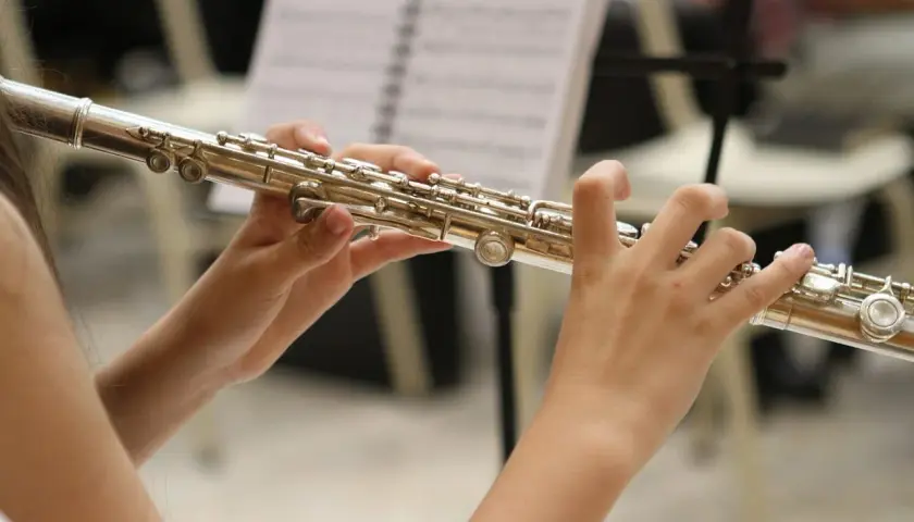 Dłonie grają na instrumencie podobnym do fletu, z nutami w tle.