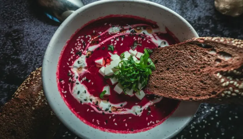 Un bol de soupe de betterave rouge polonaise, garni de crème, de dés de fromage et d'herbes, avec du pain de seigle.