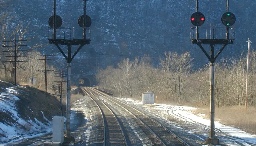 Dwa semafory kolejowe z czerwonymi i zielonymi światłami na tle tunelu i zaśnieżonego krajobrazu.