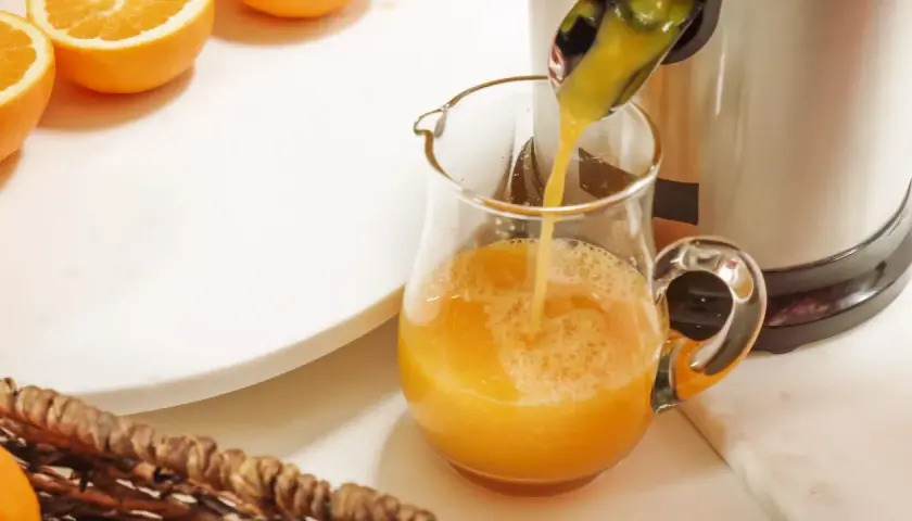 Frisch gepresster Orangensaft fließt in ein Glas. Orangen sind bereit, um zu zeigen, was man entsaften kann.