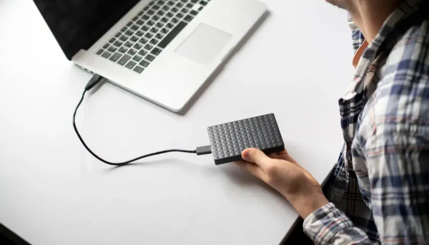 Chłopak podłącza dysk zewnętrzny do laptopa. Prosty sposób, jak podłączyć dysk zewnętrzny do laptopa, by przenieść dane.