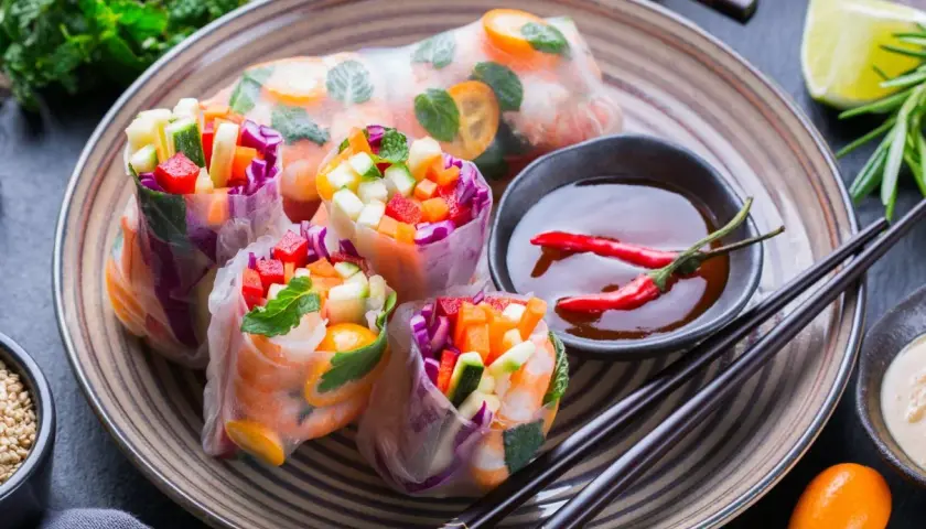Kolorowe spring rolls z krewetkami, warzywami i miętą, podane z sosem chili i limonką. Pyszna przekąska.