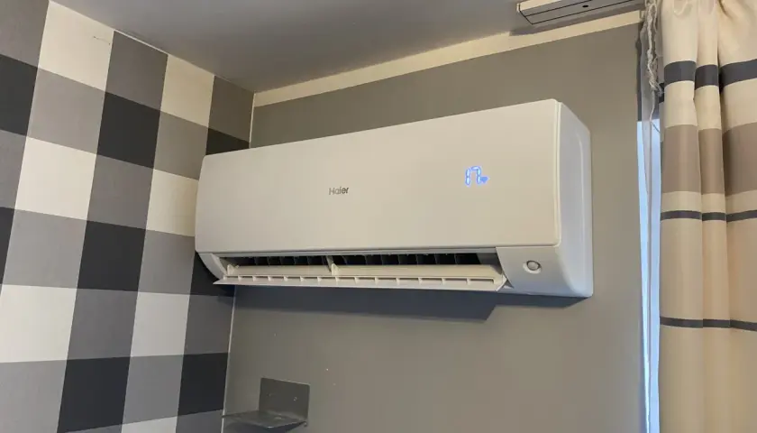 Biały klimatyzator Haier zamontowany na ścianie z szarą tapetą w kratę.