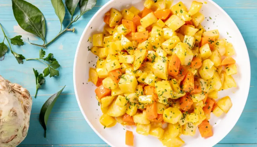 Insalata di sedano rapa e carote a cubetti, condita con erbe aromatiche. Un'idea fresca per le tue ricette crudiste.