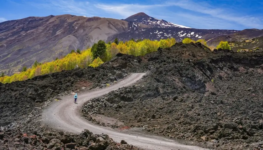 Sentiero tortuoso su Etna, ideale per una **randonnée Etna sans guide**. Paesaggio lunare con rocce laviche e vegetazione autunnale.