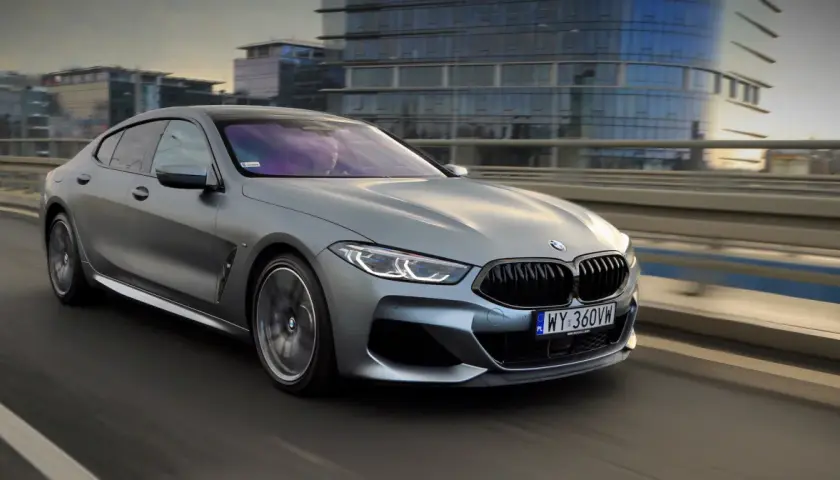 Srebrne BMW M850i sunie po moście, odbijając światła miasta w swoich lśniących szybach.