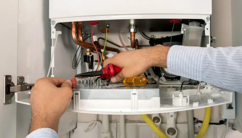 Serwisant De Dietrich naprawia kocioł, pracując przy przewodach i elementach elektronicznych.
