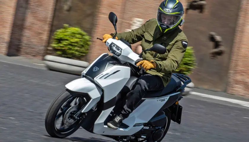 Hombre en scooter Peugeot Tweet 125, con casco y chaqueta verde, circulando por una calle.