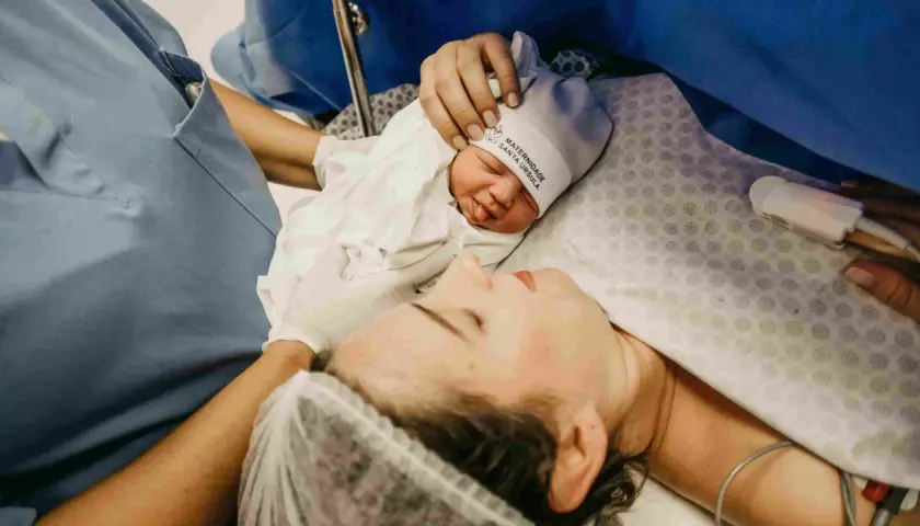 Mommy and baby bonding after cesareo. A nurse's hand gently holds the newborn's hat.