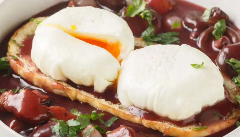 Un œuf meurette, deux œufs pochés sur toast, baignant dans une sauce au vin rouge avec lardons et oignons.