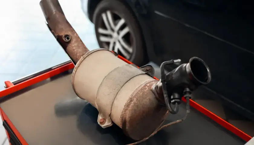 Filtr DPF na stole warsztatowym, z widocznym elementem wydechowym i złączem elektrycznym.