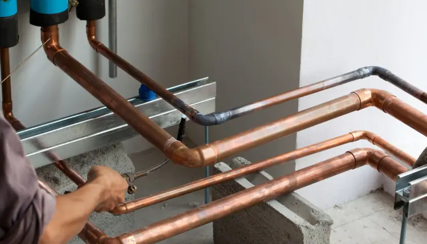 Instalator pracuje nad miedzianymi rurami, tworząc skomplikowaną sieć, niczym w zawiłych układach pole dance duety.