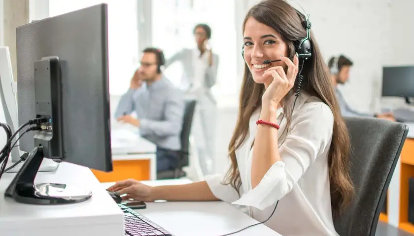 Eine freundliche Callcenter-Mitarbeiterin lächelt in die Kamera. Sie sitzt am Schreibtisch und spricht ins Headset. Sie hilft Kunden, die vielleicht auch mal Werbung widersprechen möchten.