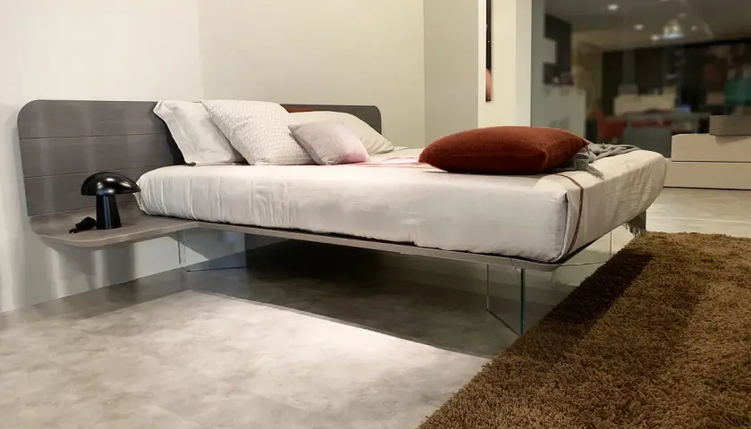 Un letto sospeso come funziona: design moderno con testiera in legno, comodino integrato e gambe in vetro trasparente.