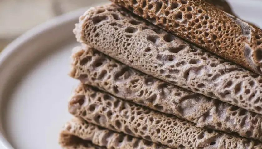 Pile de crêpes et de galettes, certaines roulées, d'autres pliées, avec une texture alvéolée. Un délice qui rappelle le goût de l'andouille.