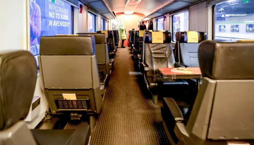 Wnętrze wagonu kolejowego, widok na miejsce połączenia wagonów. Puste siedzenia czekają na pasażerów.