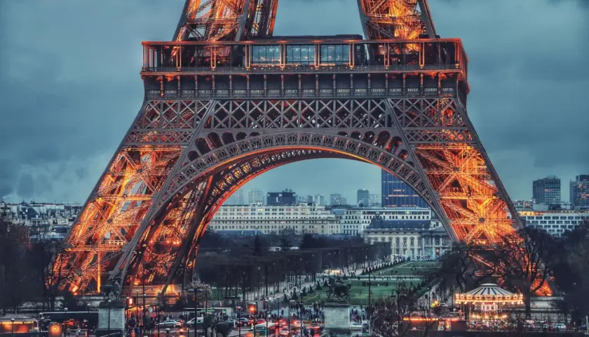 Eiffel rozświetlona pomarańczowym blaskiem, z widokiem na paryskie ulice i budynki.