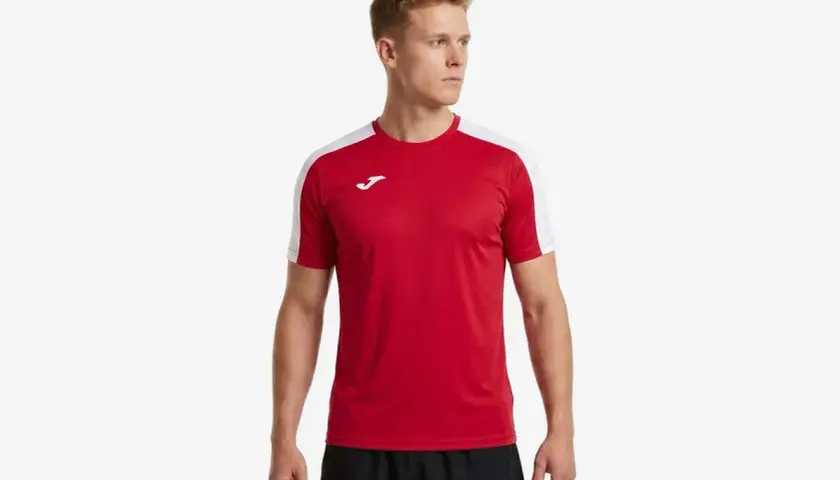 Mężczyzna w czerwonej koszulce piłkarskiej z białymi rękawami i logo Joma.