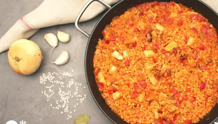 Arroz con calamares recién hecho en paellera, con ingredientes como cebolla, ajo y pimientos. ¡Un plato delicioso!