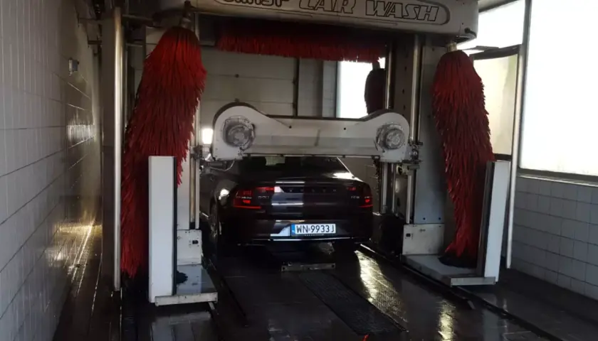 Czarny Volvo wjeżdża do myjni automatycznej. Czerwone szczotki są gotowe do pracy, pokazując, jak dobrze umyć samochód.