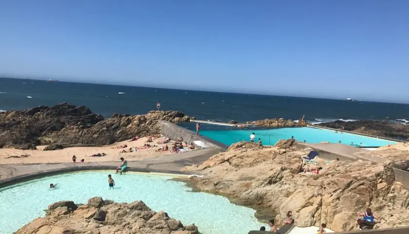 Piscinas naturais na praia de Matosinhos, Porto, com pessoas a nadar e a apanhar sol.