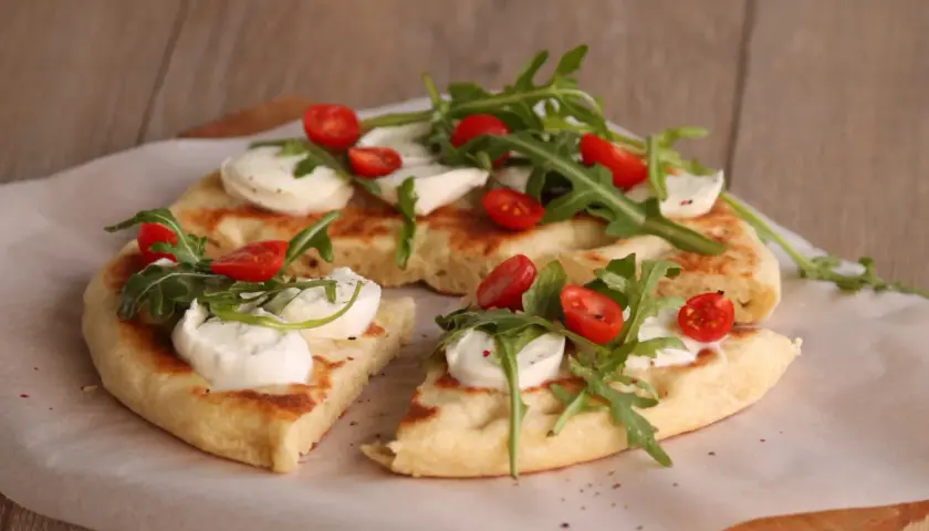 Pyszna focaccia z mozzarellą, pomidorkami koktajlowymi i rukolą, podana na papierze do pieczenia.