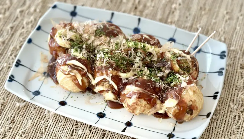 A plate of takoyaki, drizzled with sauce and mayonnaise, topped with bonito flakes and nori. Perfect for a homemade takoyaki sauce recipe.