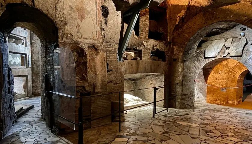 Intérieur des catacombes San Callisto. Un sarcophage blanc repose sous un arc de briques, dans un dédale de couloirs aux fresques anciennes.