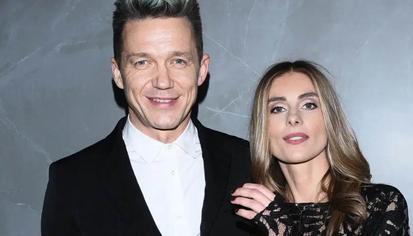 Katarzyna Zawadzka i jej mąż, uśmiechnięci, pozują do zdjęcia na tle szarej ściany.