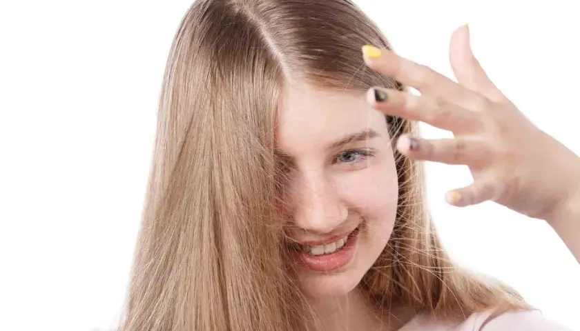 Chica sonriente con cabello rubio que se toca la frente, buscando cómo quitar la electricidad del pelo.