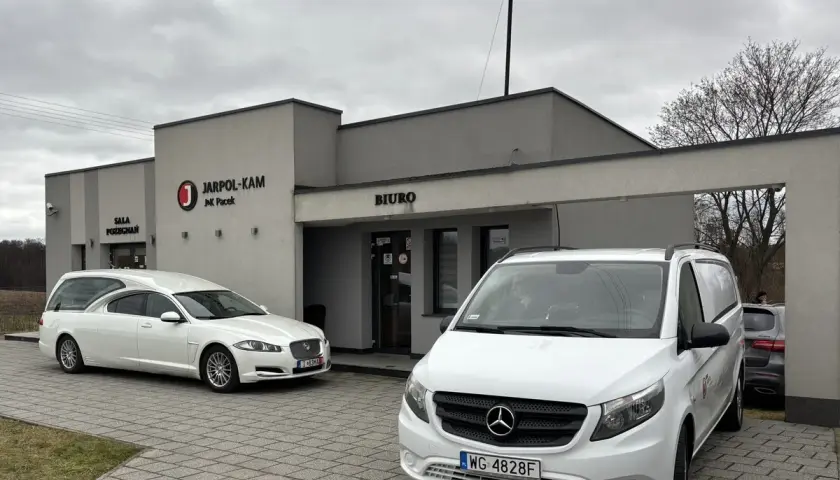 Przed budynkiem "JARPOL-KAM" stoją karawan i van. Firma zajmuje się transportem zmarłych, odpowiadając na pytanie, kto pokrywa koszty sprowadzenia zwłok z zagranicy.