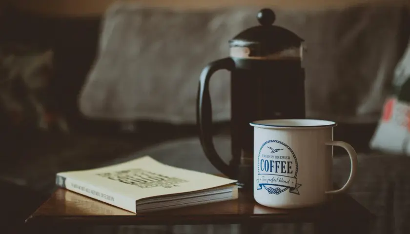 Poranna kawa z french pressa, kubek z napisem "Coffee" i książka o kawie. Idealna ilość kawy do french pressa na spokojny poranek.