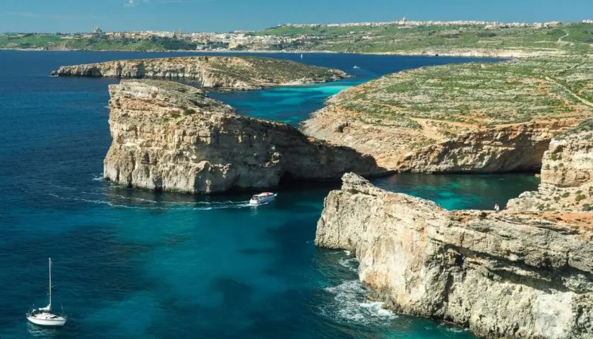 Malta zima: turkusowe wody, skaliste klify i łodzie kołyszące się na falach. W oddali widać miasto.