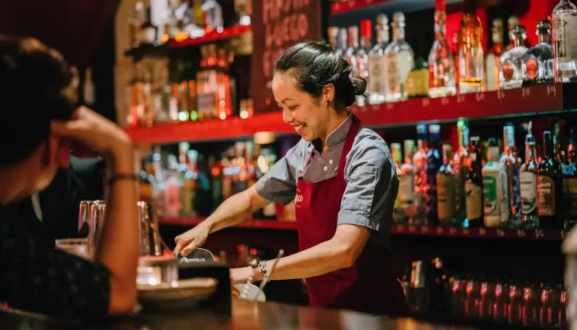 Uśmiechnięta barmanka w Gdańsku przygotowuje drinka. Zastanawiasz się, ile zarabia barman w Gdańsku?