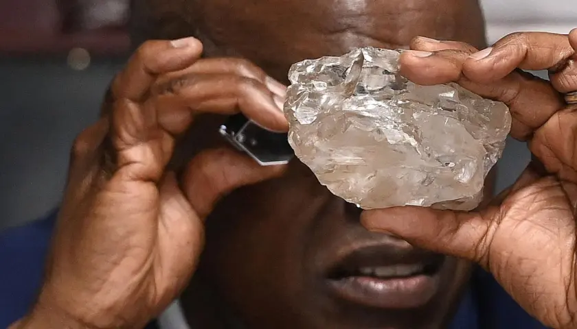 Mann betrachtet mit Lupe einen großen, rohen Diamanten. Die Frage, wie viele Diamanten es auf der Welt gibt, bleibt angesichts solcher Funde faszinierend.