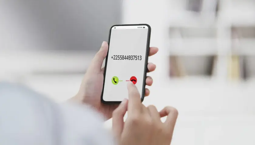 Dłoń trzyma smartfon z numerem +2255844937513. Palec wskazuje przycisk odbierania połączenia, jakby wybierał kierunkowy 40.