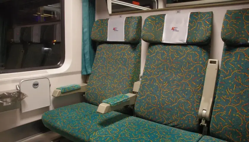 Wnętrze wagonu osobowego PKP Intercity z wygodnymi siedzeniami w turkusową tapicerkę.