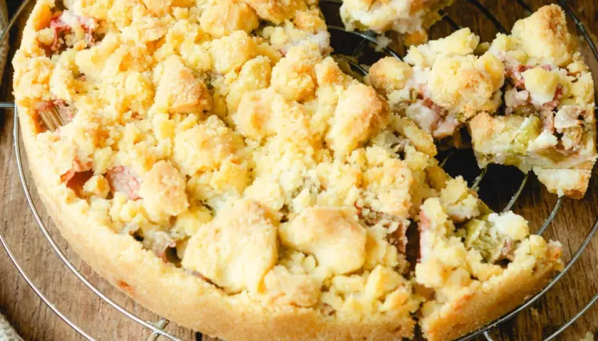 Ein köstlicher Rhabarberkuchen mit Streuseln, der auf einem Gitter abkühlt. Die süßen Streusel bedecken die saftige Rhabarberfüllung.