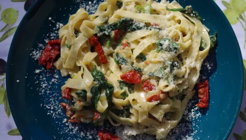 Pyszny makaron tagliatelle ze szpinakiem i suszonymi pomidorami, posypany parmezanem. Idealny na szybki obiad.