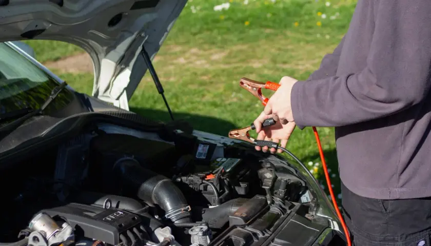 Ręce trzymające kable rozruchowe przy akumulatorze. Czy można odpalic auto na wlaczonym prostowniku?