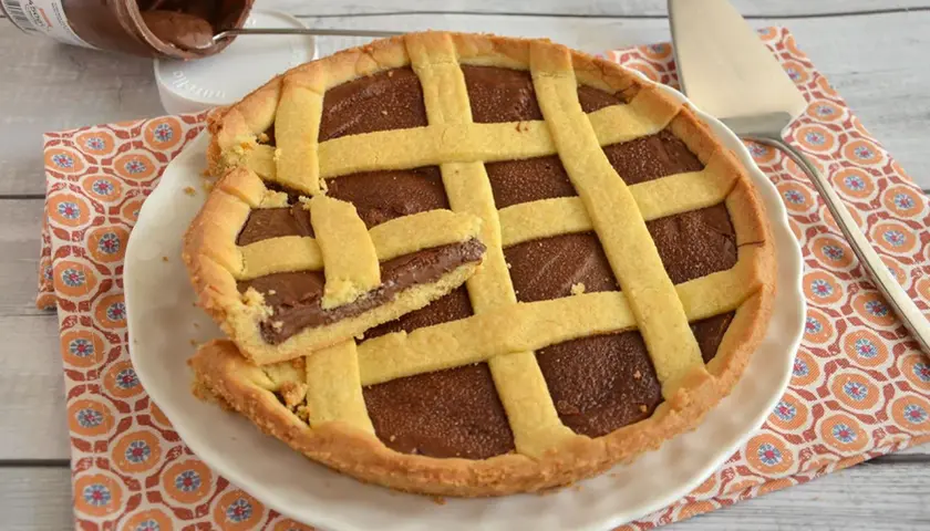 Deliziosa crostata alla Nutella con una fetta tagliata, pronta per essere gustata. Un vasetto di Nutella è visibile sullo sfondo.