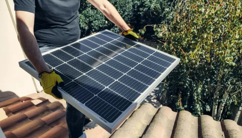 Person med gula handskar håller solpanel på taket. Undrar du vad kostar batteri till solceller?