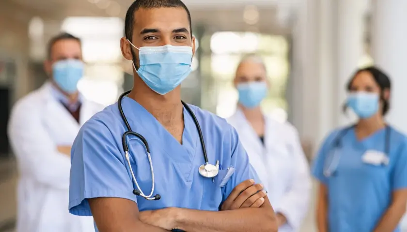 Un medico dello sport sorride, con colleghi sullo sfondo. Lo stipendio di un medico dello sport è una ricompensa per la dedizione.