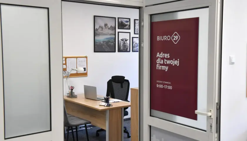 Widok biura rachunkowego z biurkiem, laptopem i tablicą ogłoszeń. Na drzwiach widnieje logo i godziny otwarcia.
