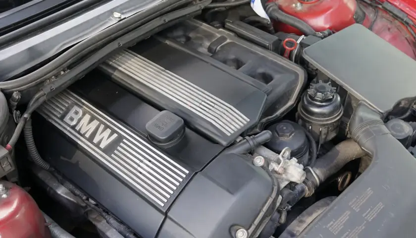 Silnik BMW e46, widok z góry. Czarna pokrywa silnika z napisem BMW i metalowymi wstawkami. Widać też elementy układu dolotowego i zbiorniczek płynu.
