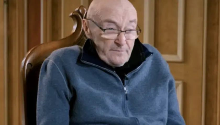 Phil Collins, zmagający się z chorobą, siedzi w fotelu, ubrany w niebieski polar.