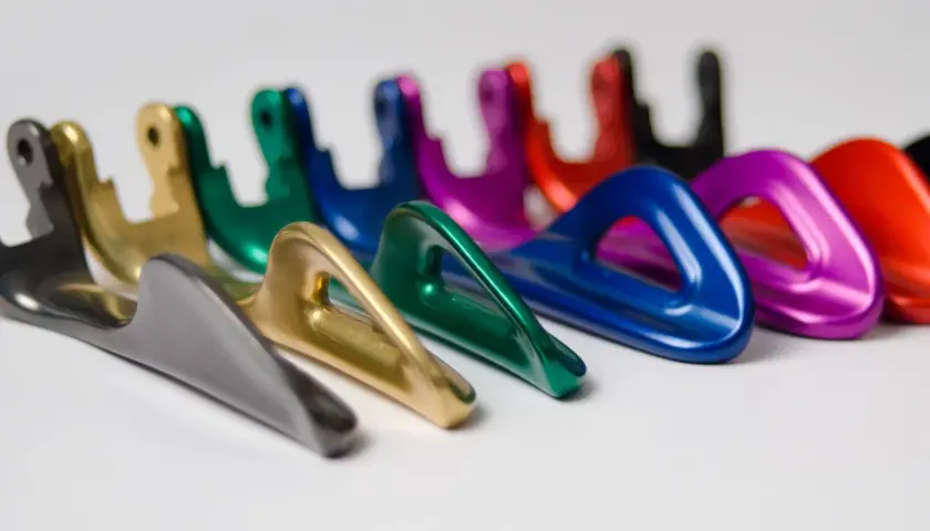 Una fila di moschettoni colorati, con finitura anodizzazione naturale, disposti su sfondo bianco.