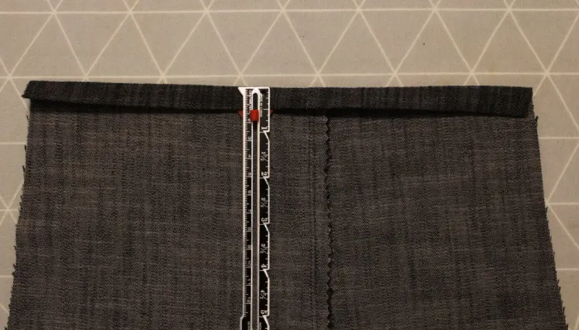 A ruler measures a dark grey cotton twill fabric. The fabric has a visible weave, characteristic of what is cotton twill.