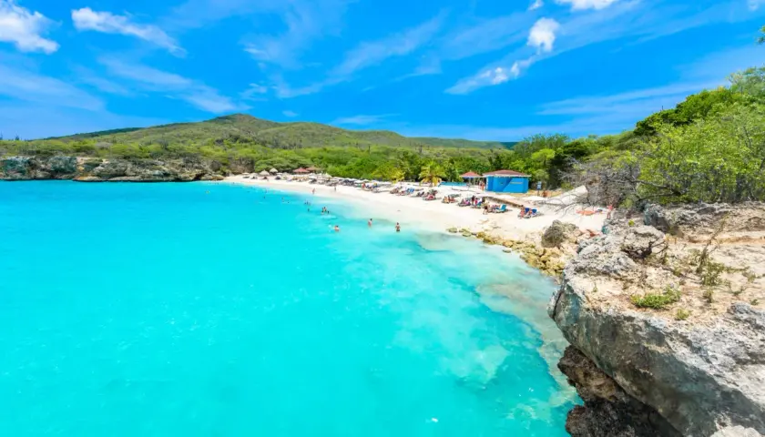 Traumhafter Curacao Beach mit türkisblauem Wasser, weißem Sand, Liegestühlen und Menschen, die schwimmen und sich sonnen.